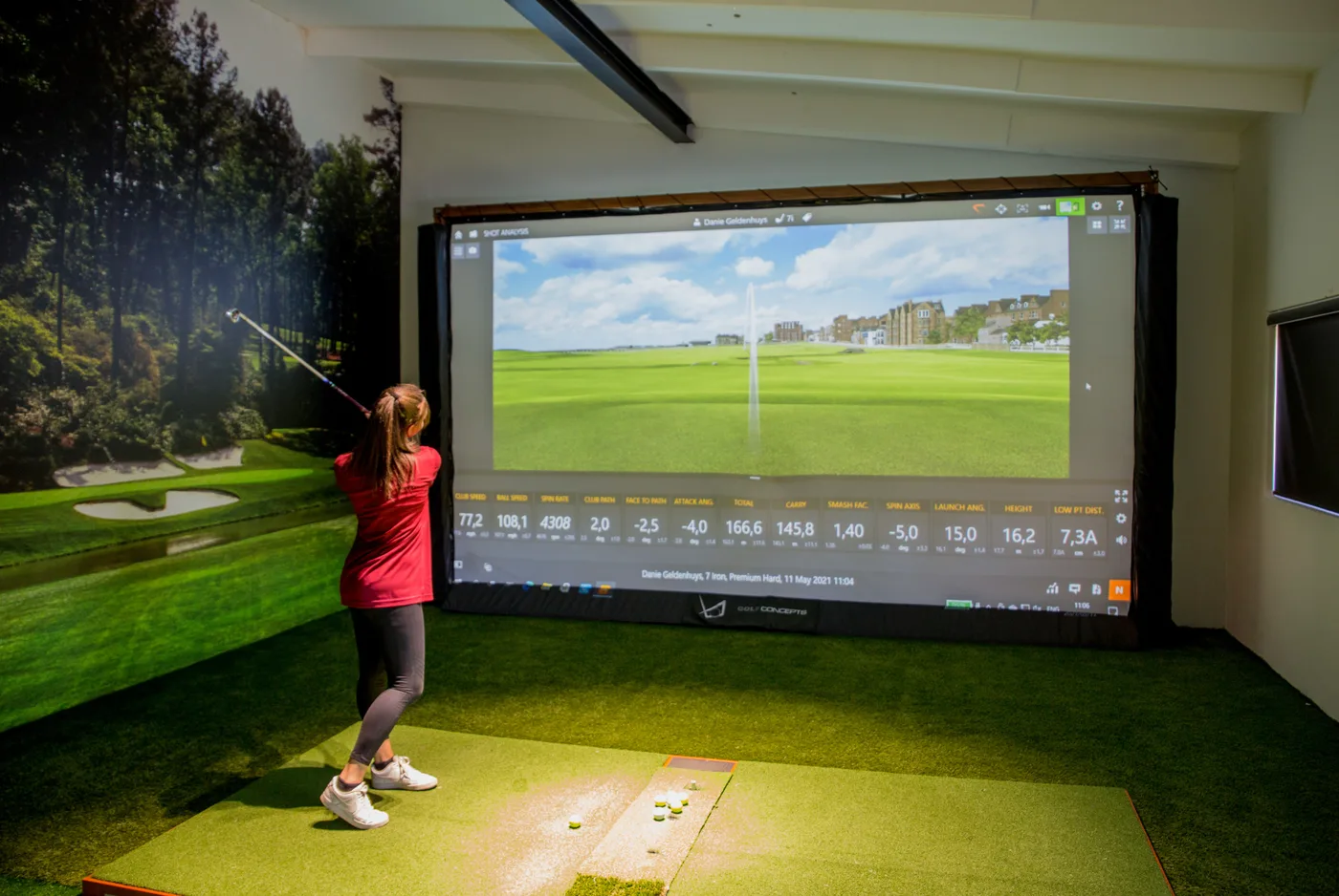 A golfer following through in the Golf Concepts fitting bay, with the full TrackMan readout on the screen behind