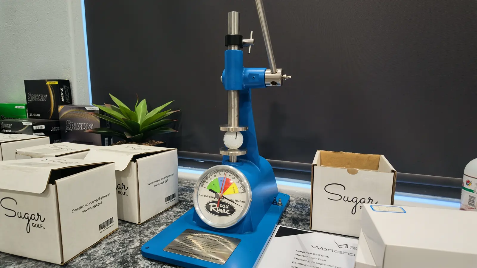 The ball compression tester on the counter at Golf Concepts, beside boxes of Sugar Golf balls