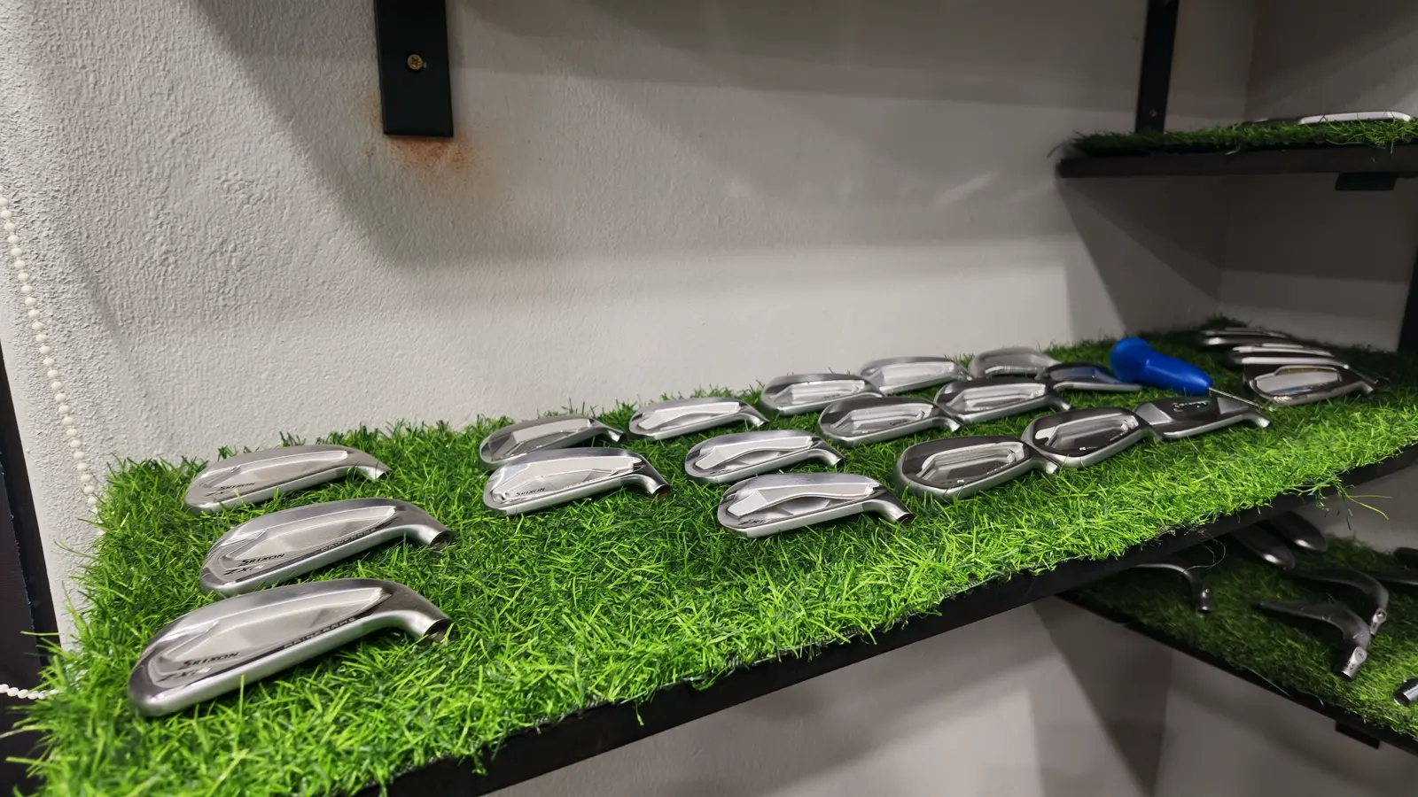 A full set of iron heads laid out on the turf bench at Golf Concepts