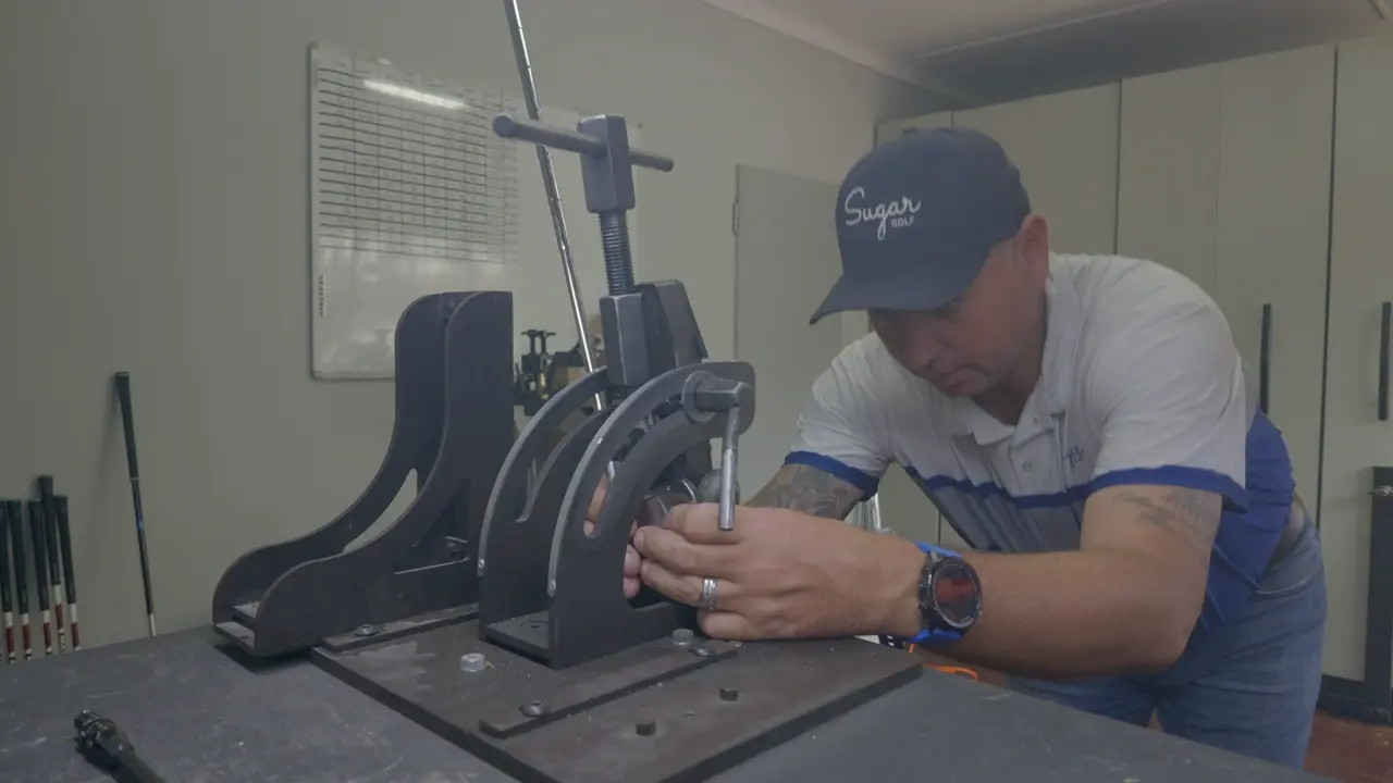 An iron clamped in the bending machine on the workshop bench at Golf Concepts